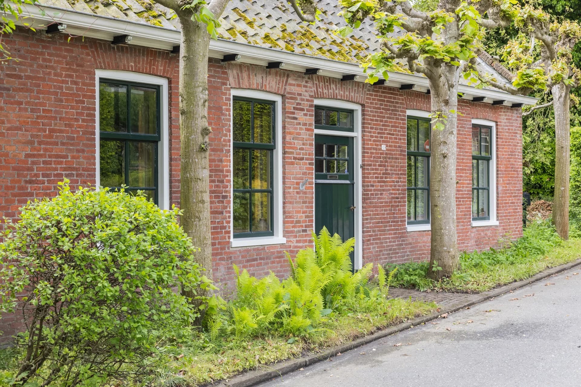 Karaktervolle bakstenen boerderij aan straatkant met groene tuin, vastgoedfotografie Friesland