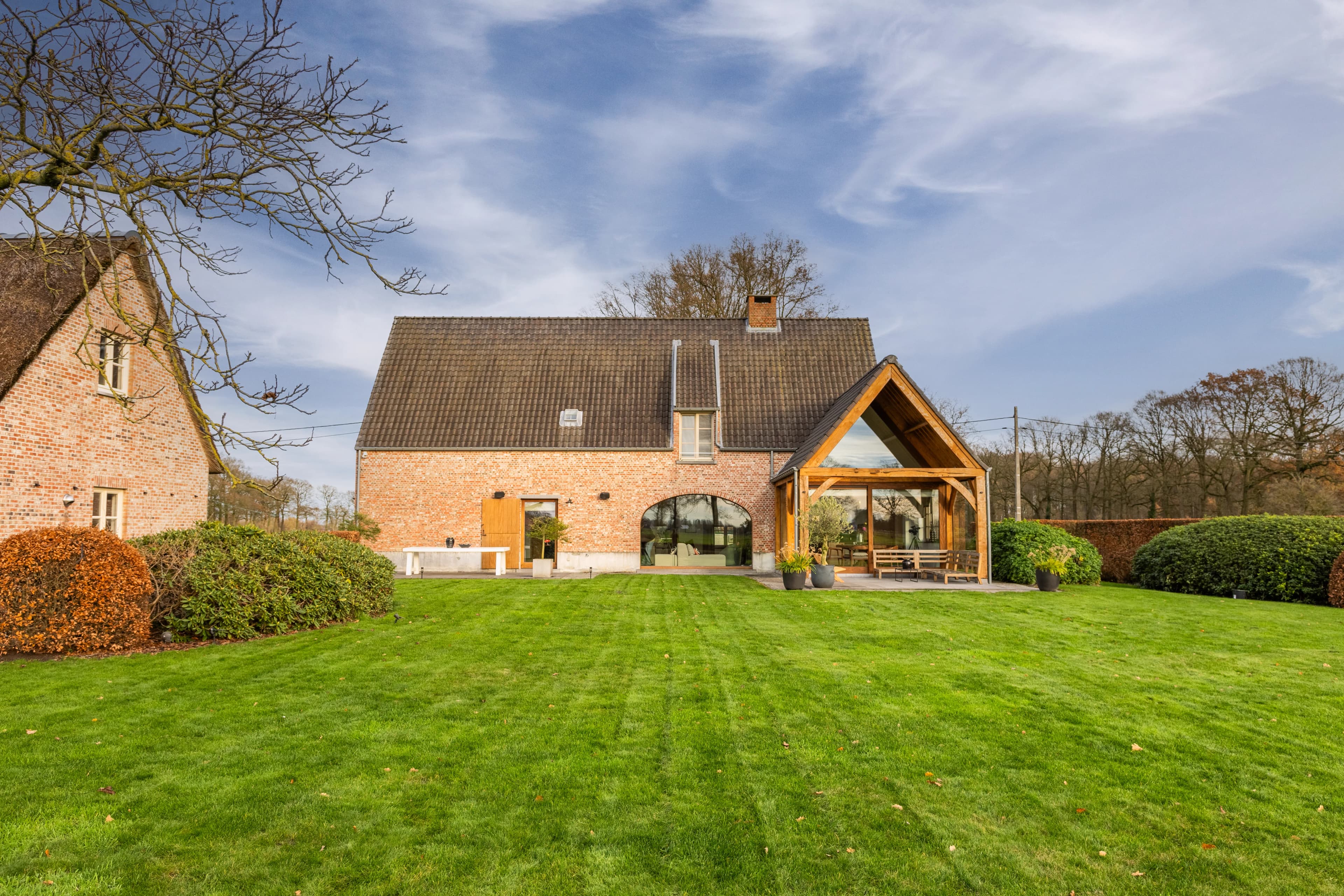 Boerderij achterzijde met grote gazon en houten overkapping in herfstlicht, vastgoedfotografie