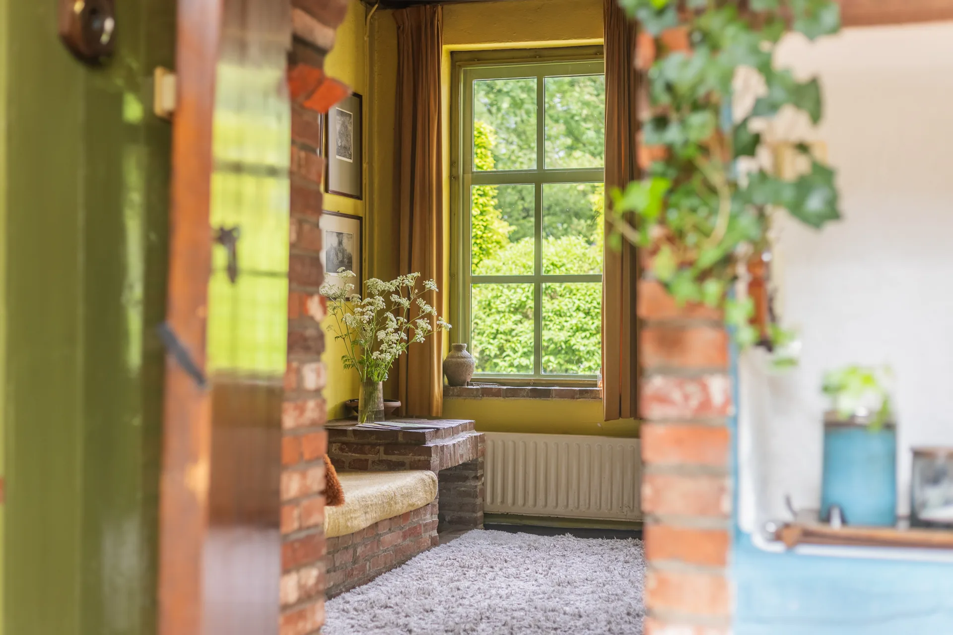 Doorzicht door hal naar tuinvenster in karaktervol interieur met baksteendetails, vastgoedfotografie