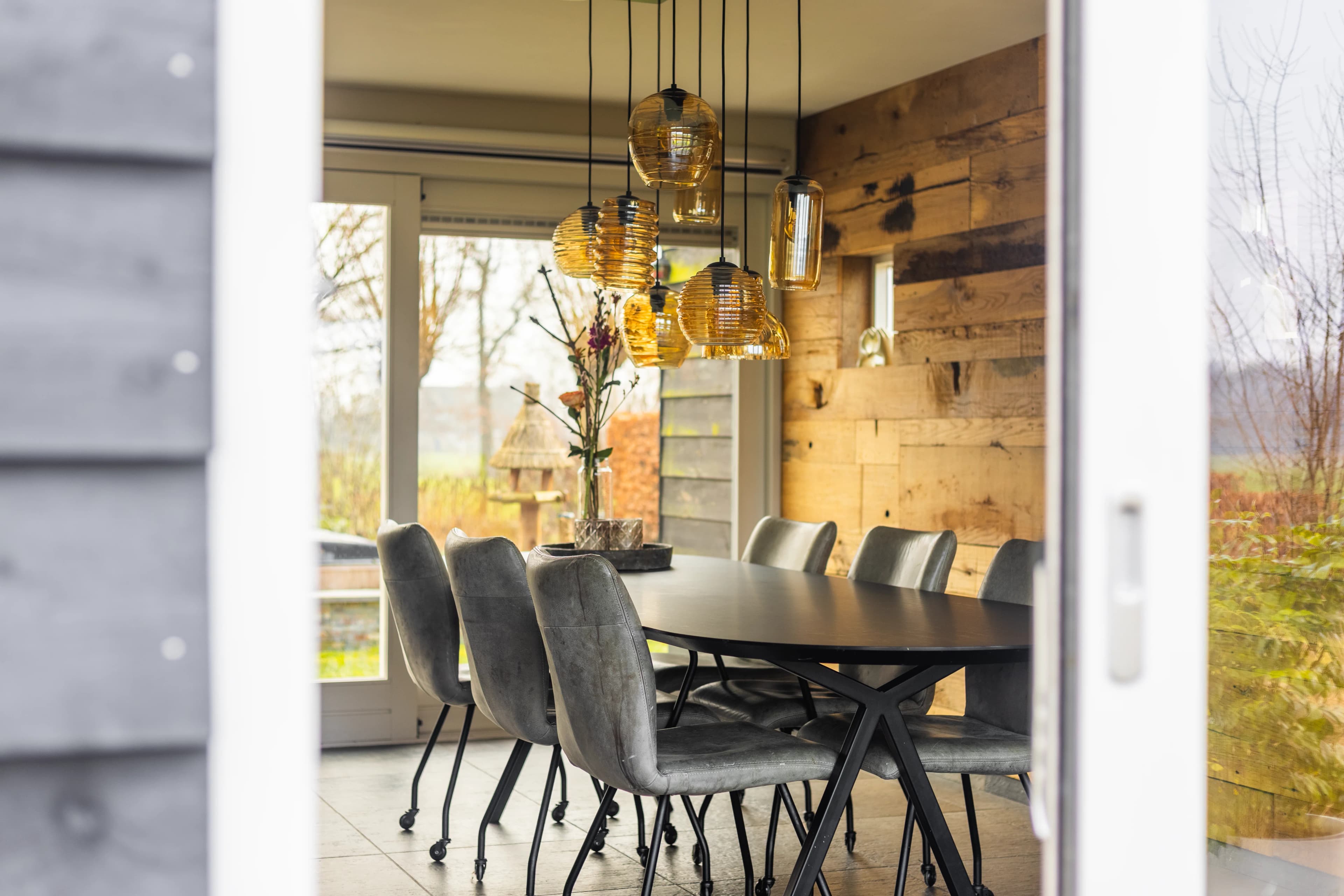 Eetkamer gezien door glazen deur met warme houten wand en hanglampen, vastgoedfotografie