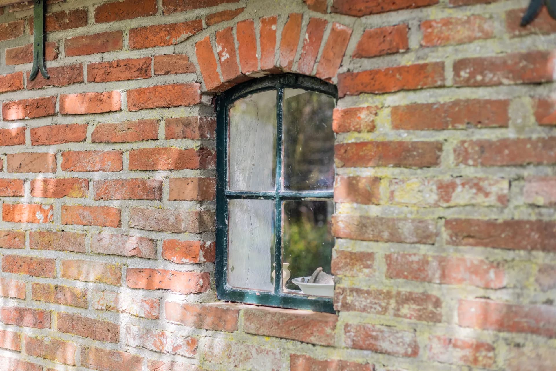 Historisch gietijzeren raam in verweerde bakstenen gevel, sfeer detail vastgoedfotografie