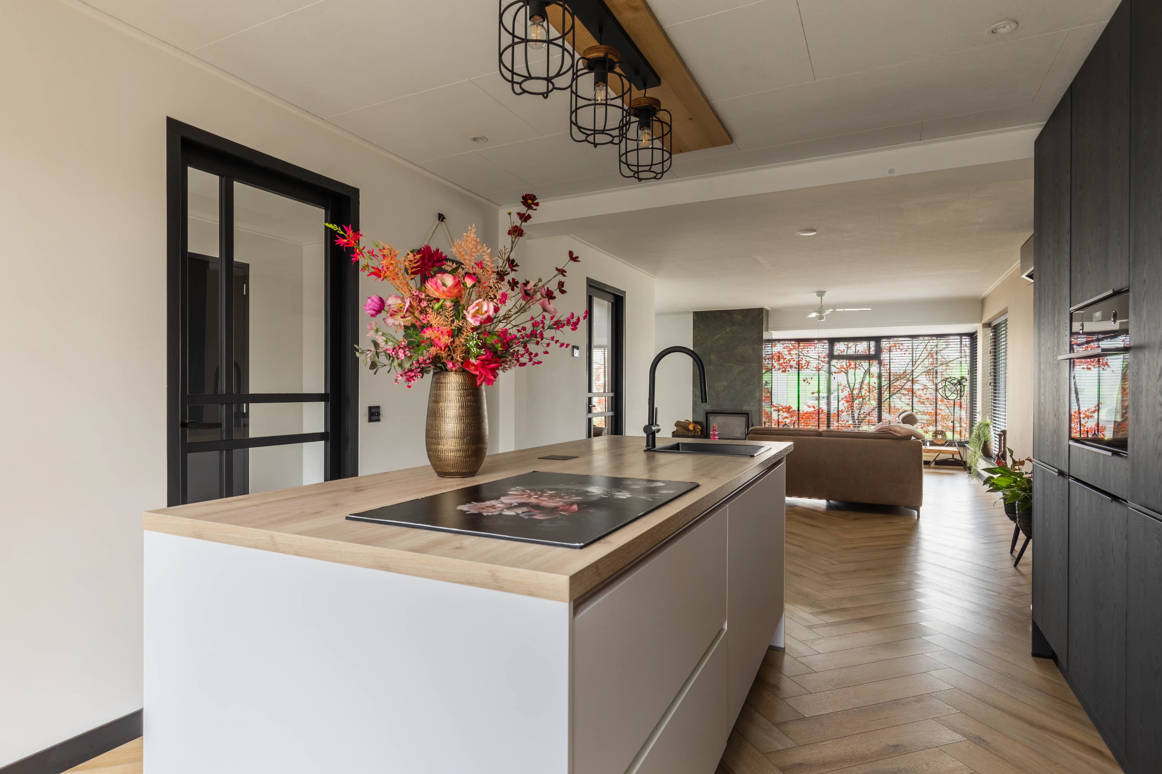 Moderne open keuken met eiland, bloemstuk en doorzicht naar woonkamer, vastgoedfotografie