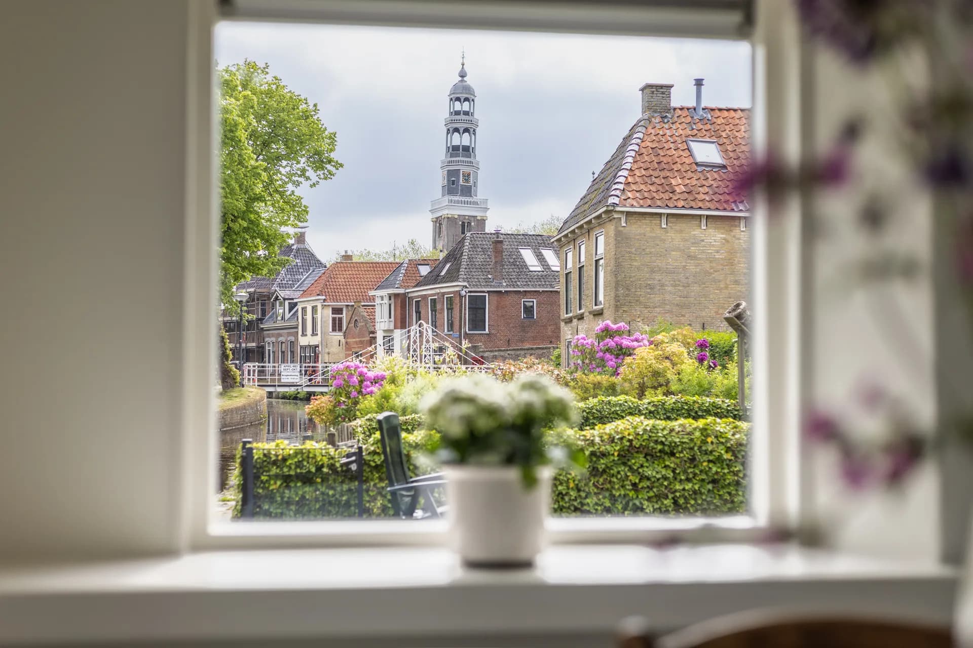 Uitzicht door raam op Friese kerktoren en gracht met bloeiende tuin, vastgoedfotografie