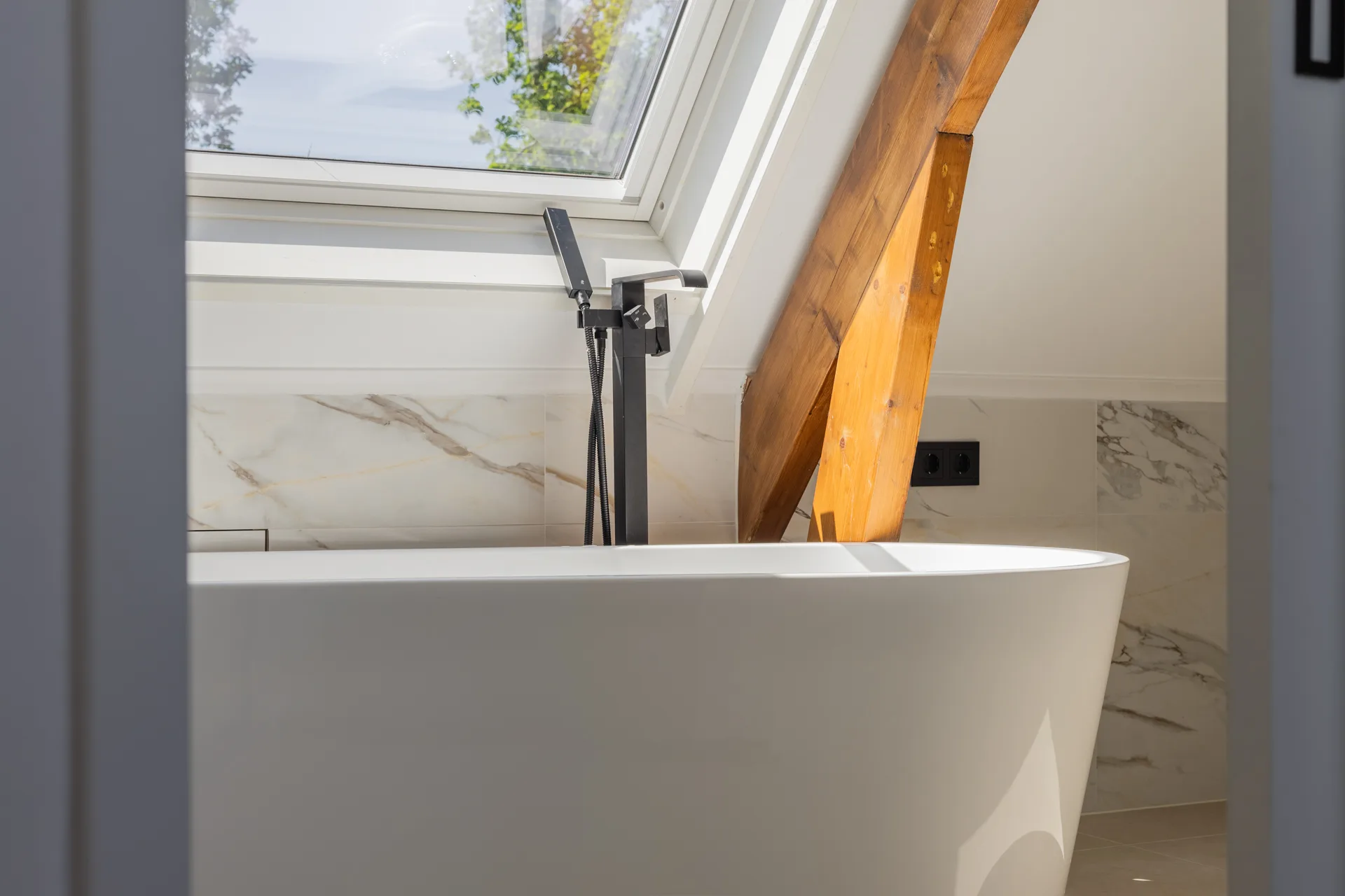 Vrijstaand bad naast dakraam met houten kapbalk, detail interieur vastgoedfotografie