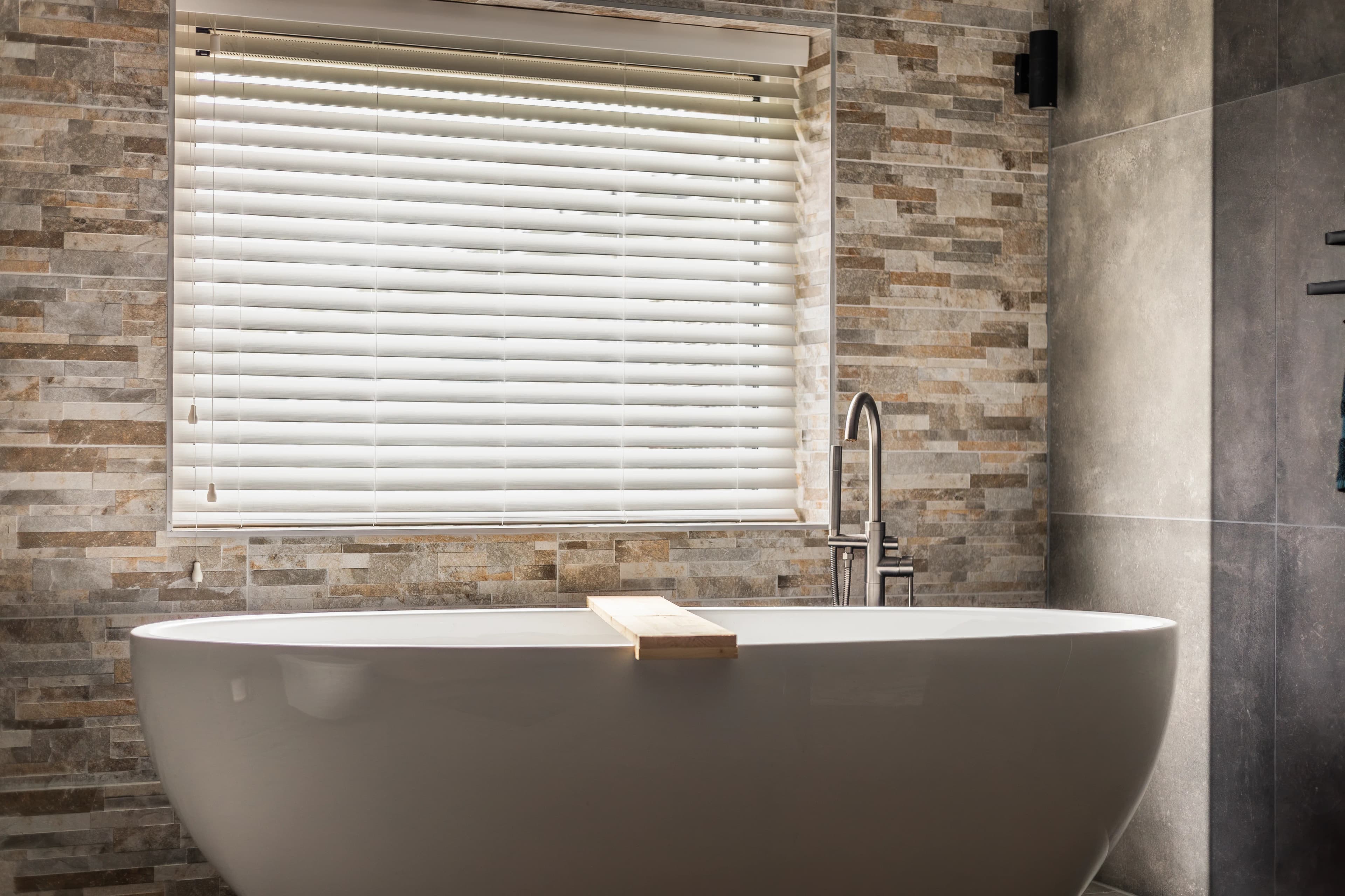 Vrijstaand bad met natuursteenstructuur en raam, luxe badkamer vastgoedfotografie