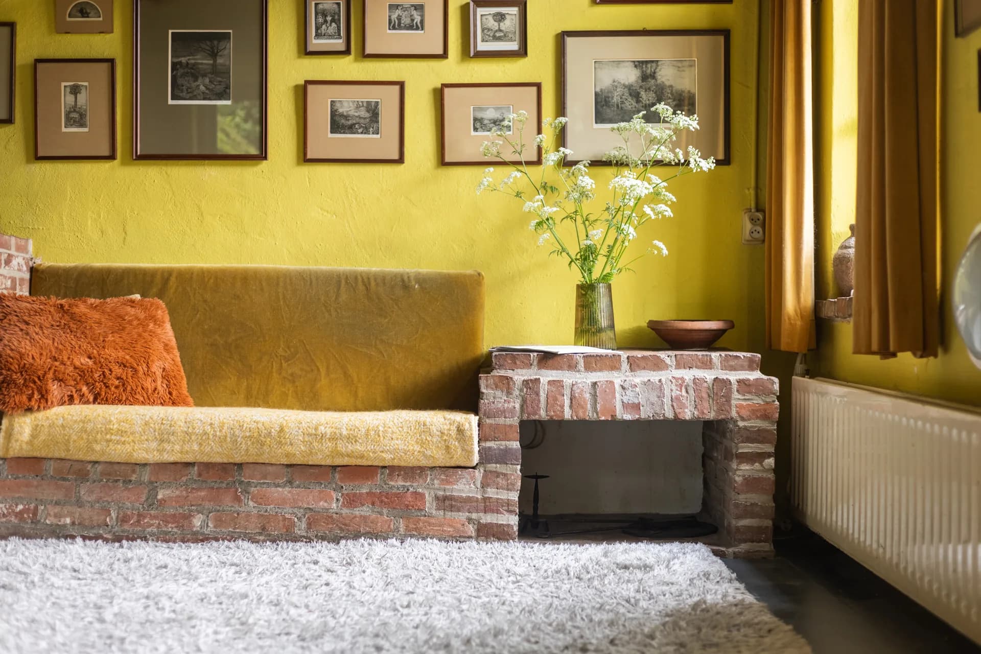 Retro woonkamer met gele wand, bakstenen zitbank en open haard, sfeer vastgoedfotografie